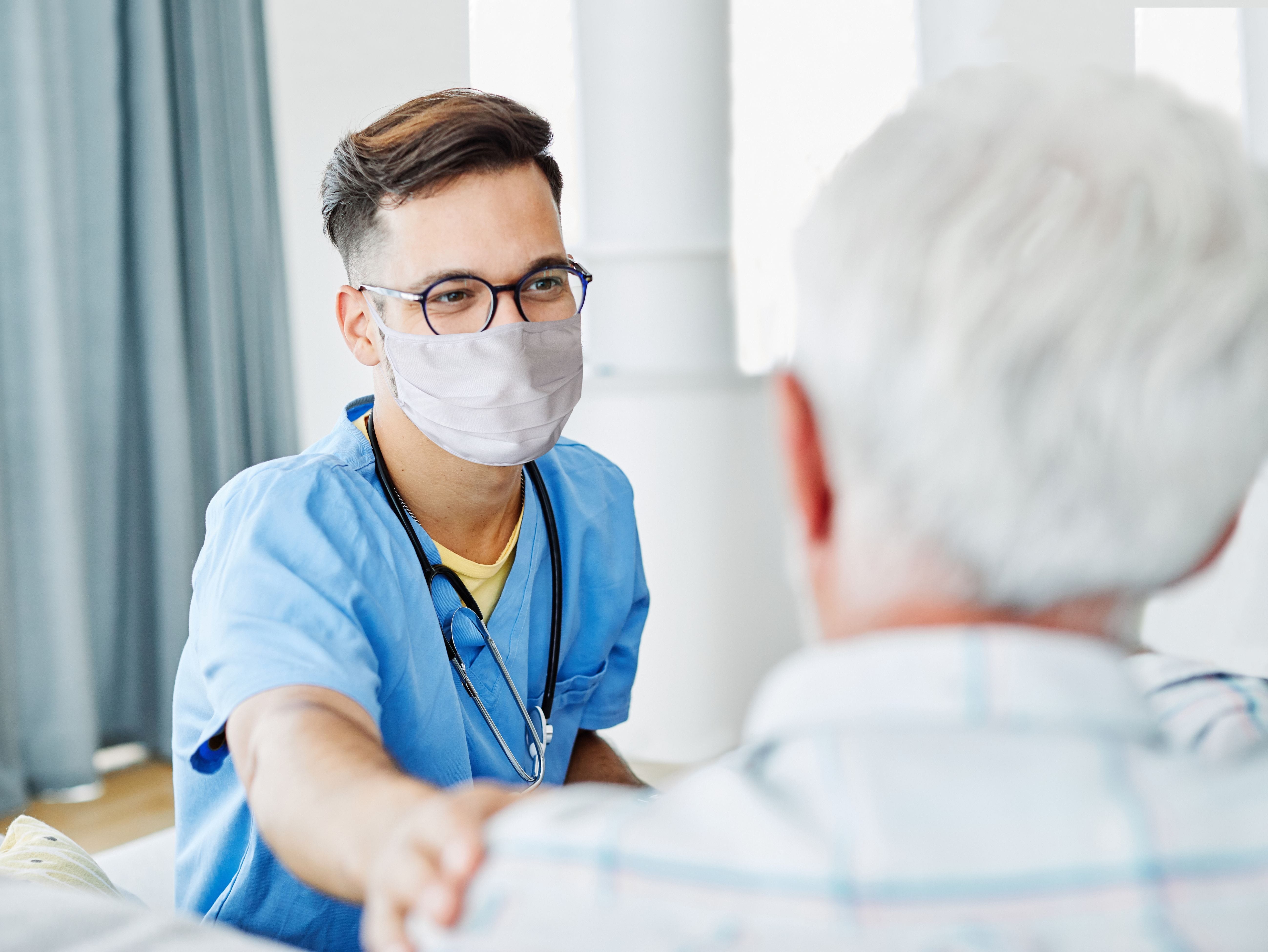 Nurse talks to patient with mask on Nurse has hand on patient's shoulder as nurse talks to patient with a mask on