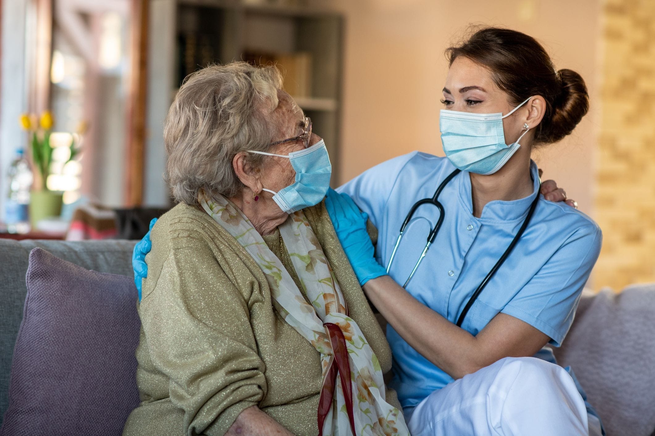 Nurse sitting on the couch with patient Nurse sitting on the couch with a patient in her home while wearing masks.