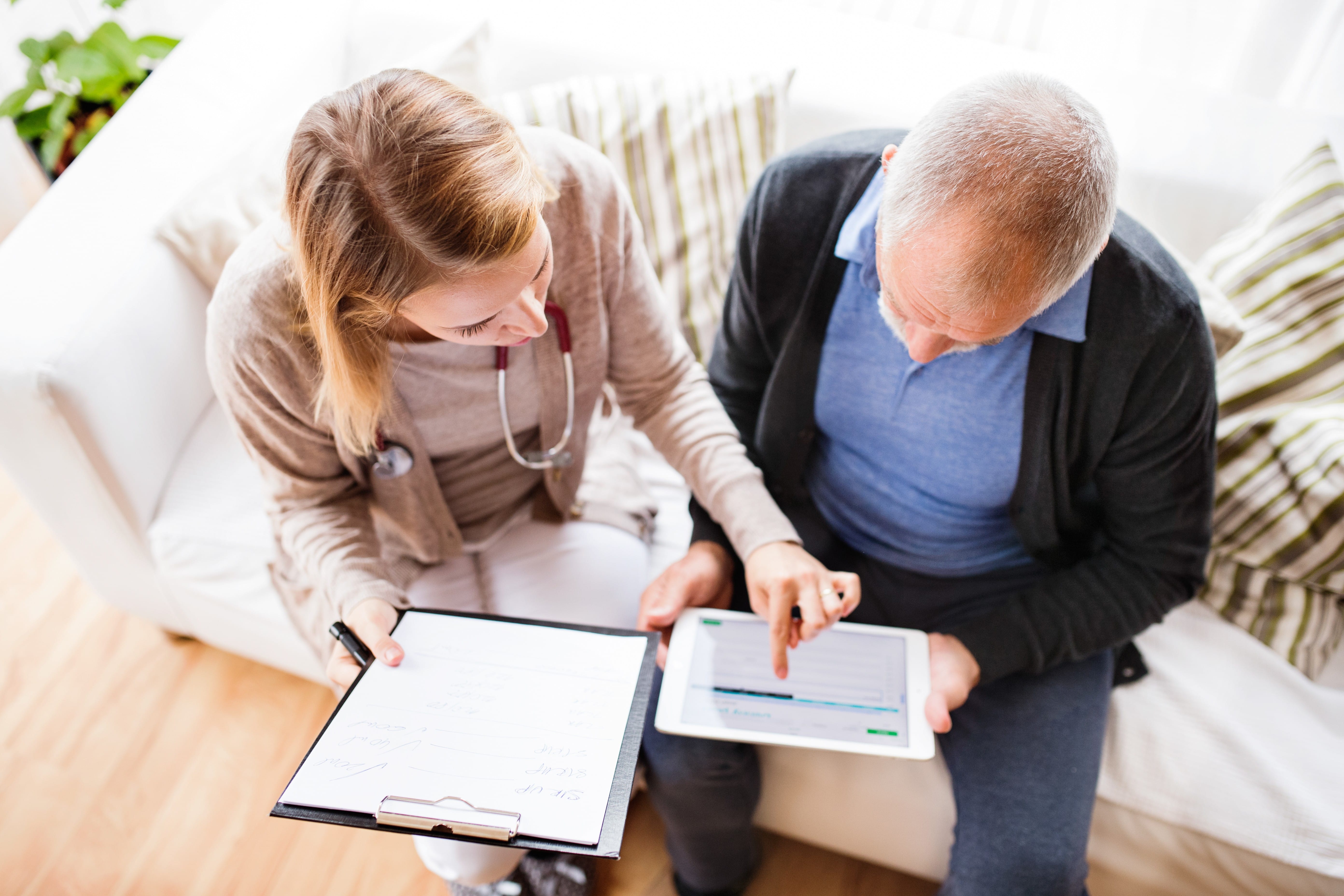 Nurse pointing to screen while holding clipboard Nurse pointing to screen while holding clipboard while sitting on couch.